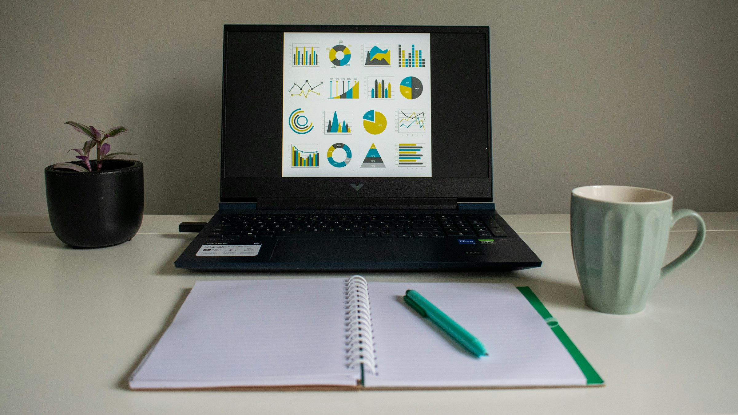 Laptop displaying business charts beside an open notebook